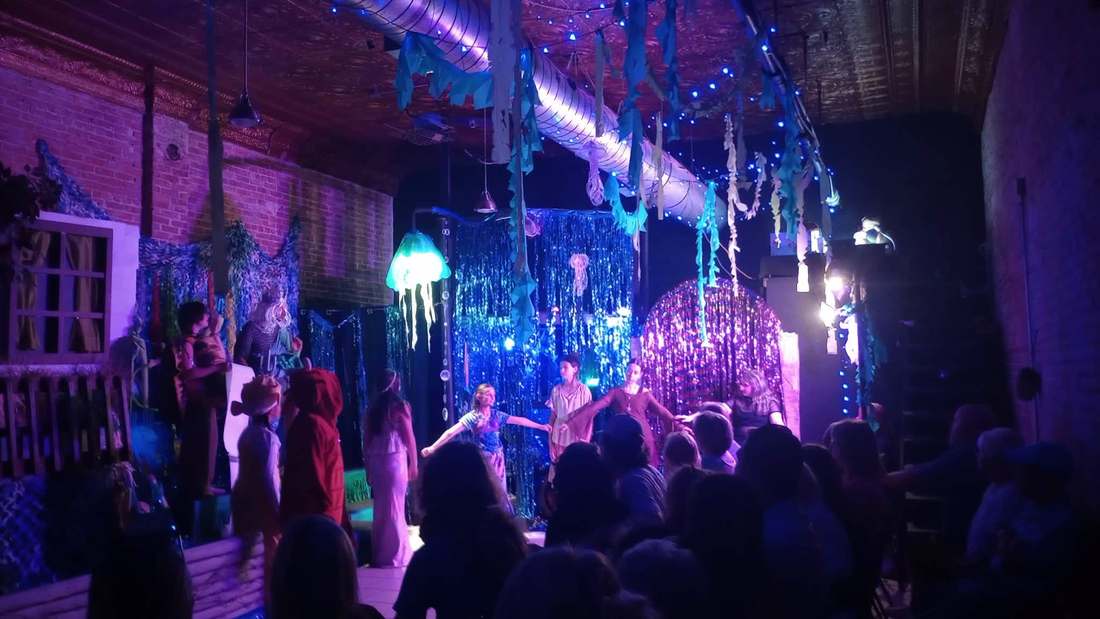 The Little Mermaid cast performing on a wide stage surrounded by an underwater set