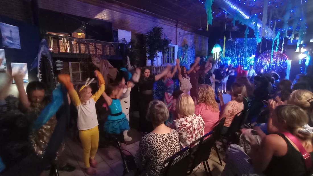 Children dancing with costumed cast members on opening night in the underwater-decorated venue