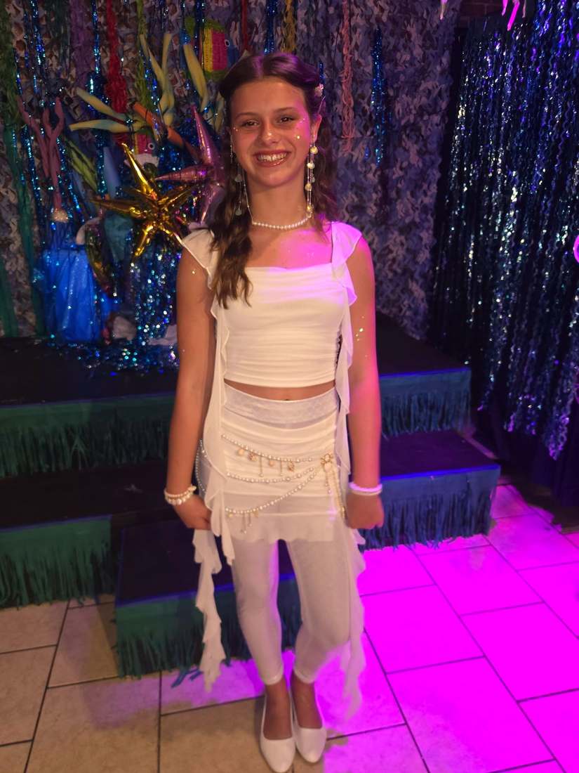 A mermaid sister in a white costume posing before the underwater set