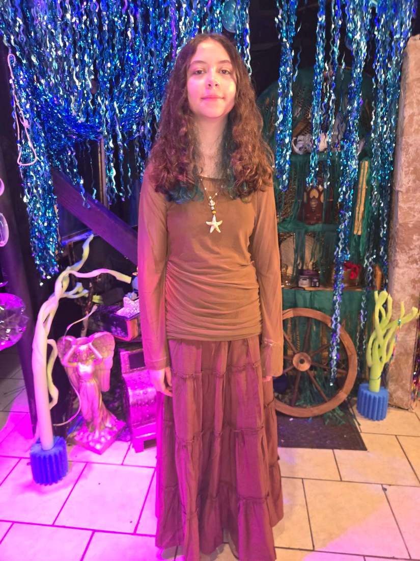 A Little Mermaid cast member in a brown top and white tiered skirt wearing a starfish necklace