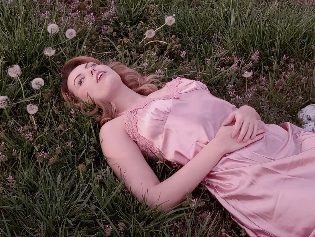 Bonnie lying in the grass among dandelions in a pink satin dress