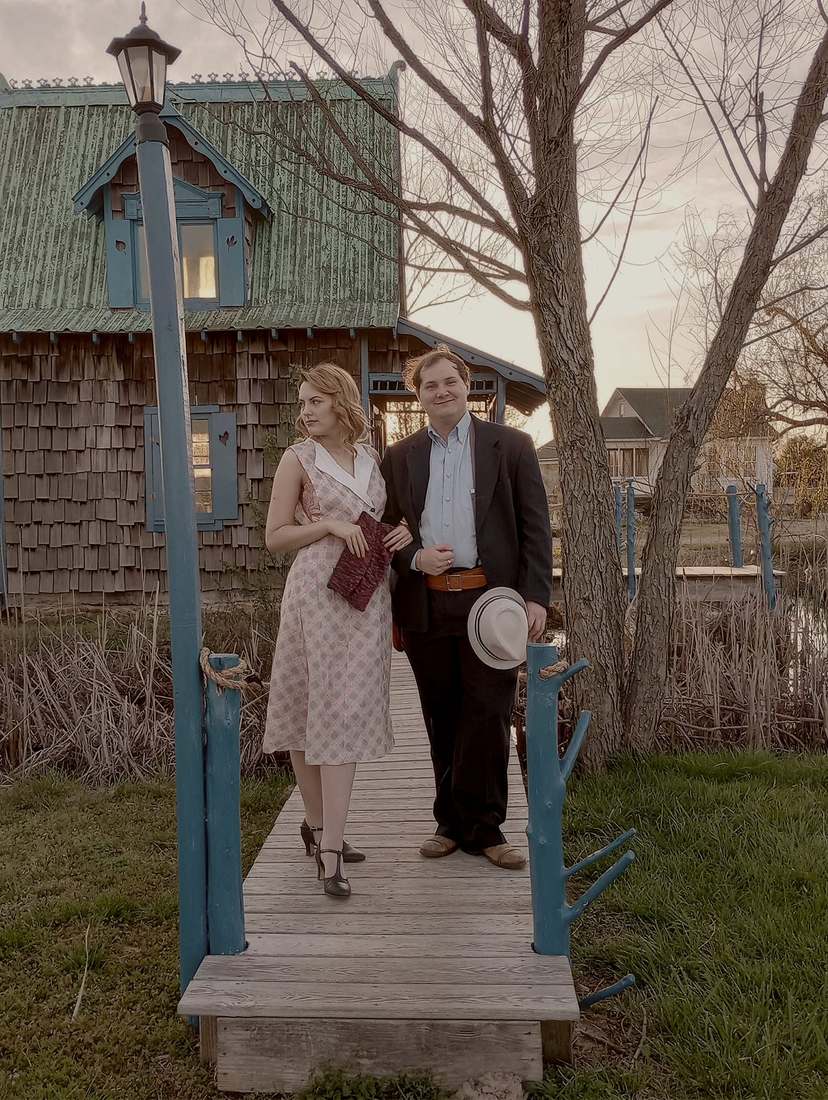 Bonnie with a cast member on a wooden footbridge in front of a shingled cottage