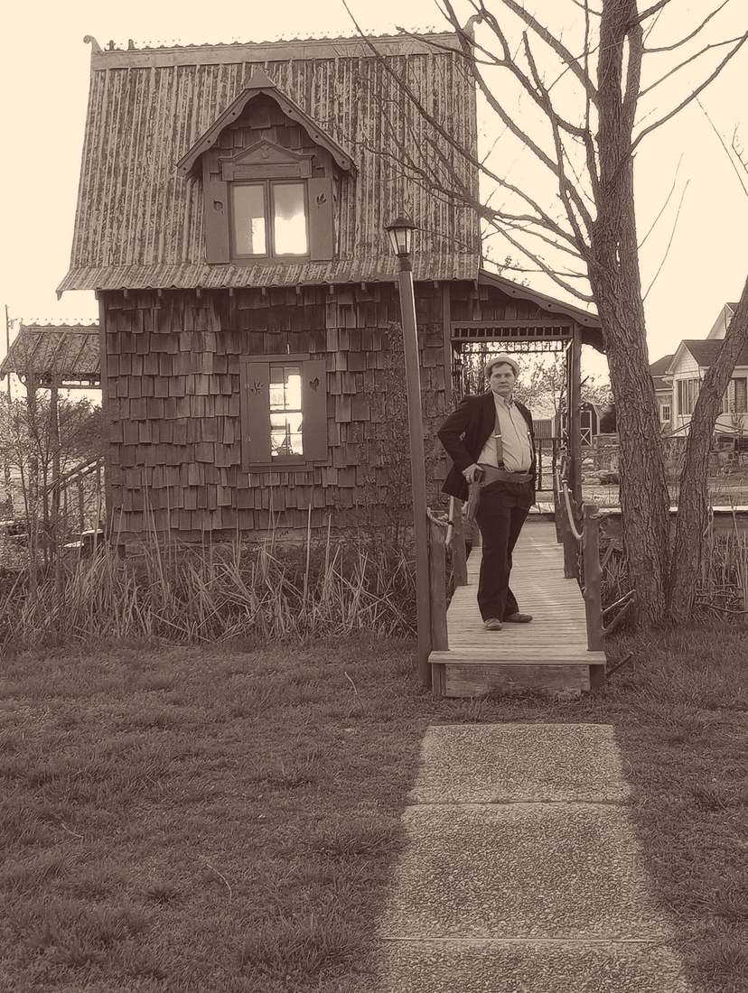 A cast member standing on the footbridge in front of the shingled cottage (sepia)