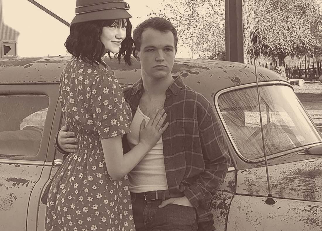 Two cast members embracing beside the vintage car (sepia)