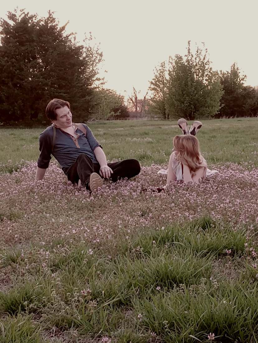 Bonnie and Clyde facing each other in a field of pink wildflowers at sunset