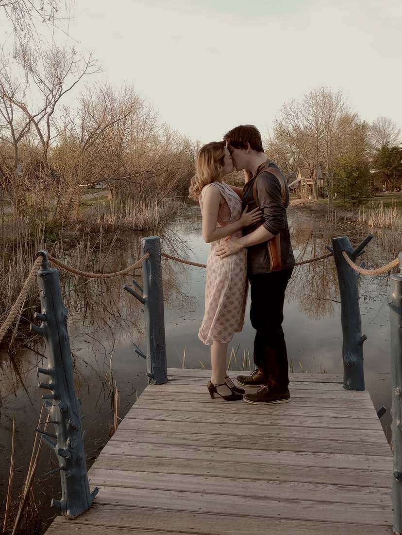 Bonnie and Clyde kissing on a wooden dock over a pond