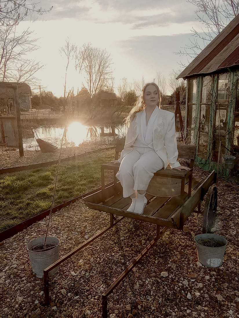 A cast member in a white suit sitting on a wooden cart by the pond at sunset