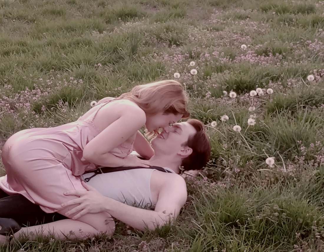 Bonnie leaning over Clyde in a field of dandelions, close up
