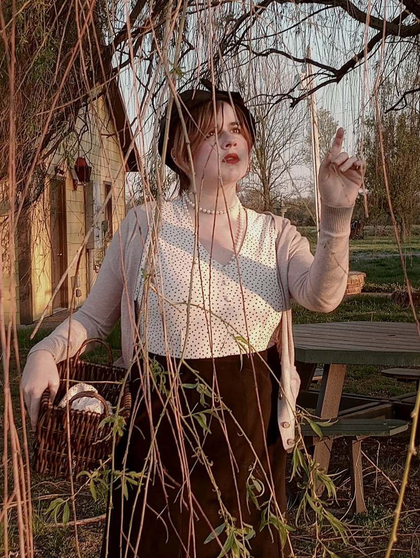 A cast member holding a wicker basket beneath willow branches