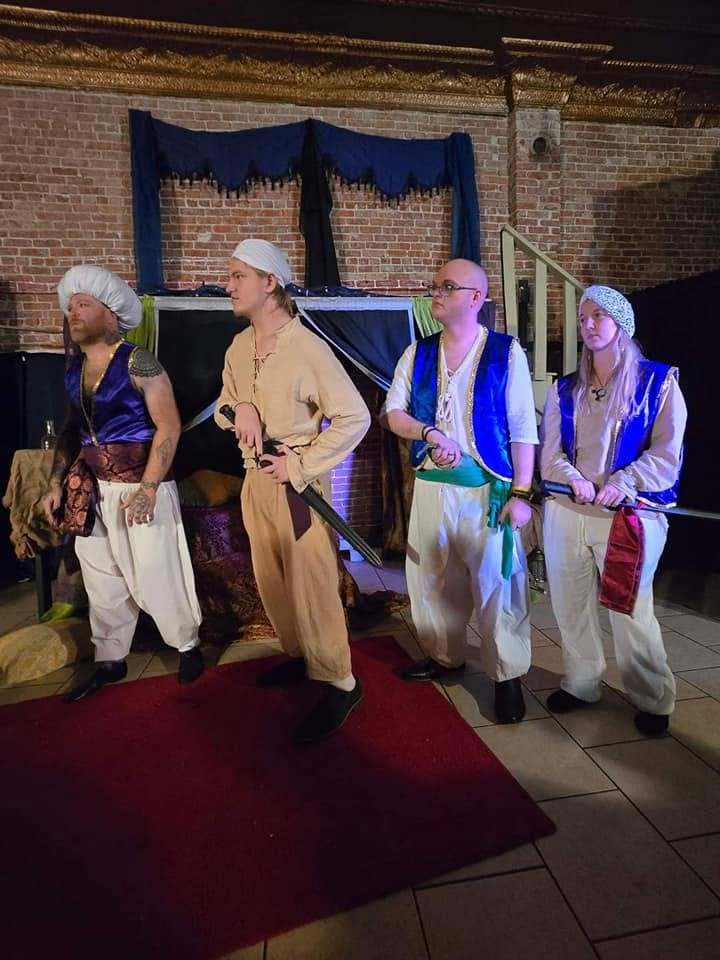 Four palace guards in vests and turbans stand at attention, swords at their belts, in Twisted