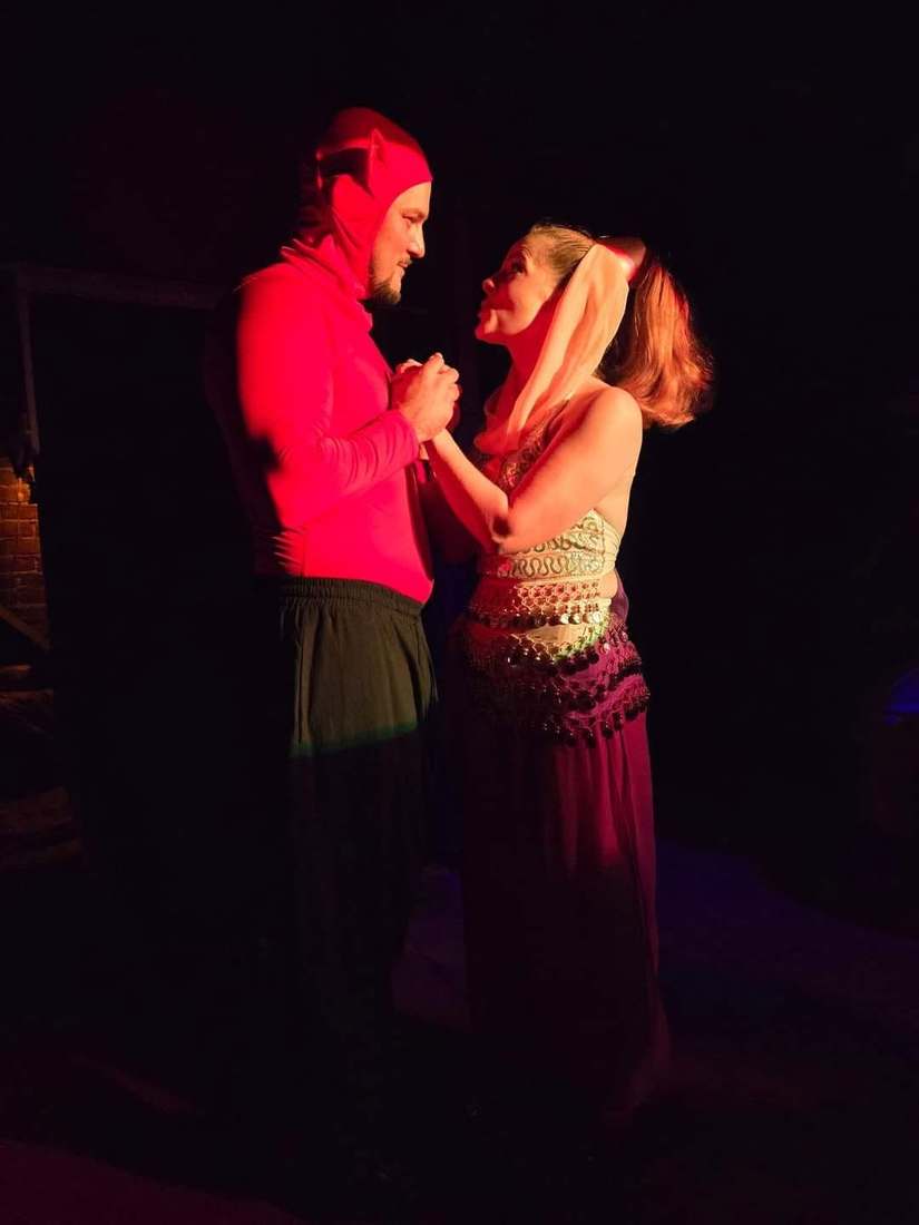 Two performers clasp hands in near-darkness under red light in Twisted